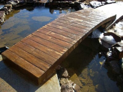 Boardwalk wood stamp (BW170) created this cool bridge. Job by Baltz and Son. Wood stamped concrete bridge spanning small pond